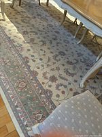 Photo of a large wool rug under a dining room table and chairs showing the detailed floral vine pattern in cream and blue tones.