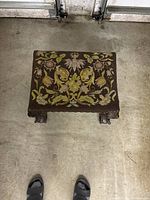 Top-down view of the mahogany footrest bench showing the intricately woven floral tapestry upholstery on the top and carved claw-style feet.