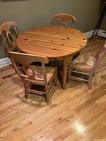 Photo of a round wooden game table with four matching wooden chairs placed around it on a wood floor.