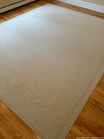 Photo of a large rectangular grey wool rug placed on hardwood floor near a window, showing the whole rug and its texture.