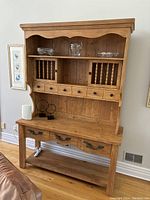 Front view of large wooden hutch showing upper open shelves, vertical slat compartments, middle small drawers, lower work surface with three large drawers, and open bottom shelf.