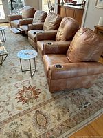 Five-piece brown leather sectional sofa with reclining footrests and integrated cup holders on armrests. Arrangement shows the sectional connected on a decorative floral area rug.