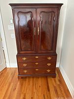 Front view of Thomasville mahogany armoire showing two paneled doors with brass hardware and three drawers below.