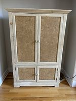 Front view of the painted pine storage cabinet with closed doors showing distressed white paint and panel design.