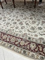 Photo showing a close-up view of the kitchen dining rug highlighting the beige field with floral details and the distinctive red accent border with ornate designs.
