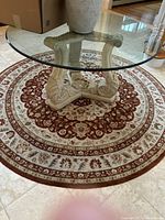 Round patterned rug with red and cream floral design under a glass table