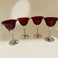 Four ruby red glass martini cocktail glasses with twisted chrome stems and chrome bases arranged in a line.