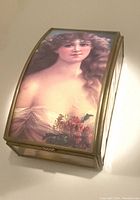 Front angled view showing curved glass top with portrait of a lady wrapped in flowers, metal frame and clear glass sides