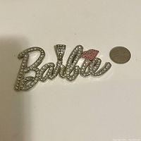 Barbie pendant front view with clear rhinestones and pink lips detail, next to a quarter for size.