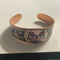 Photo showing copper cuff bracelet with colorful Native Haida art featuring a face and geometric patterns.