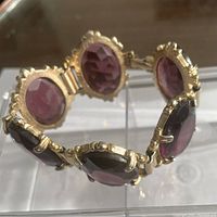 Close-up of the gold tone metal bracelet showcasing the large purple faceted glass stones and prong settings with decorative beads.