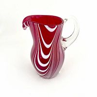 Side view of red and white swirl art glass jug with clear glass handle showing flowing design and shape.