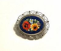 Oval flower mosaic brooch set in a silver tone filigree frame, showing detailed craftsmanship and floral colors.