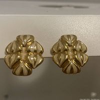 Front view of gold tone enamel clip-on earrings showing floral or abstract petal design with cream enamel inlays.