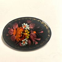 Top view of the oval black wooden brooch with colorful floral handpainted design and gold border.