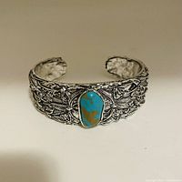 Front view of silver tone cuff bracelet showing detailed engraved pattern and central turquoise stone.
