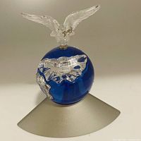 Swarovski crystal figurine of a clear dove bird on top of a blue globe with silver continents, mounted on a curved silver base.