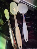 Overview of 3 cooking spoons: small solid spoon, medium and large perforated spoons on black stovetop