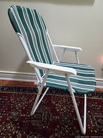 Side view of folding chair showing white metal frame and green and white striped fabric upholstery.
