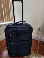 Full front view of navy blue luggage with extended telescopic handle and visible zipper compartments and compression strap.