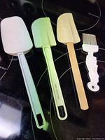 Three silicone mixing spatulas and one silicone pastry brush arranged on a stovetop.