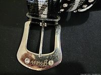 Close-up of silver buckle with two embedded rhinestones and engraved script brand logo.