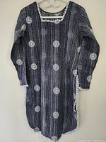 Full view of black casual dress with white embroidery and long sleeves hanging on white hanger