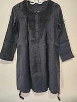 Full view of black women's casual dress hanging on a hanger showing front buttons, long sleeves, and lace detailing on neckline.