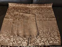 Four silk fabric samples laid out, showing brown floral and butterfly jacquard pattern and pinked edges.