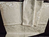 Set of three beige or cream fabric samples featuring a floral jacquard pattern, edges pinked, folded and laid out flat to show full size.