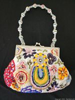 Full view of the small handbag showing multicolored floral embroidery with beads and sequins on a white fabric base, silver frame, and beaded handle.