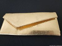 Closed view of the gold metallic purse, showing envelope style flap and textured surface.