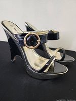 Pair of black patent leather wedge sandals showing gold-tone buckle strap and metallic gold insole.