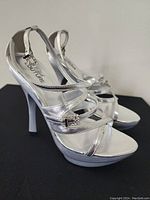 Side view of one silver high heel sandal showing strap details and stiletto heel