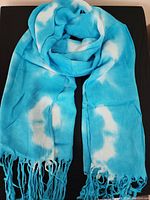 Turquoise and white tie-dye scarf with fringed ends laid flat showing texture and color pattern.