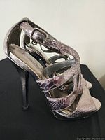 Side view of one shoe showing metallic snake print, buckle strap, and stiletto heel.
