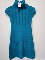 Full front view of teal cable knit sweater dress with two front pockets and short sleeves.
