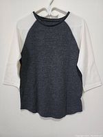 Front view of a new women's two-tone sweater, dark gray body with white sleeves on a hanger.