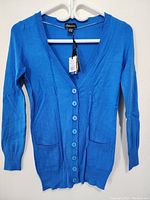Front view of women's blue knit sweater cardigan with buttons and two front pockets, size XS, on hanger with tags attached.