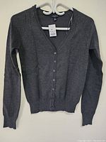 Full view of the women's grey open front sweater hung on a hanger, showing front button closure and long sleeves.