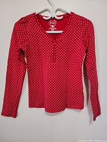 Front view of a red women's long sleeve top with white polka dots hanging on a white hanger