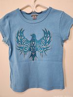 Full front view of a light blue women's short sleeve top with glittered bird design.