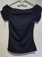 Front view of a black women's top hanging on a plastic hanger, showing an off-shoulder style with ruched puff sleeves and gathered bust detail.