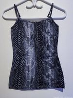 Front view of women's sleeveless snake print top hanging on white hanger against a white wall.