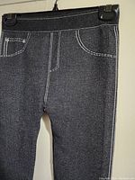 Close-up showing texture and white contrast stitching on dark gray leggings pants with faux pockets and seams