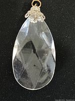 Close-up photo of a clear, diamond cut, teardrop-shaped pendant against a black background.