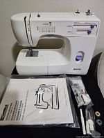 Photo of Kenmore sewing machine with owner's manual and a clear plastic bag with various accessories on the table.