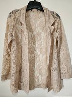 Full front view of the beige floral lace dressy top on a hanger showing long sleeves and open front.