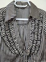 Front view showing black and white vertical stripes, ruffled trim along neckline and front, large pointed collar