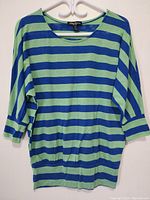 Full front view of women's striped knit top in green and blue, hanging on white hanger.